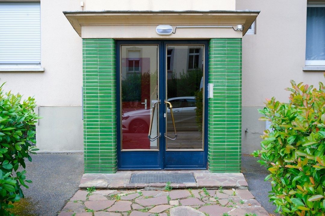 Porte vitrée d’immeuble à double battant, encadrée de briques vertes